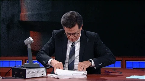 Stephen Colbert sorts through a large sheet of printed paper.