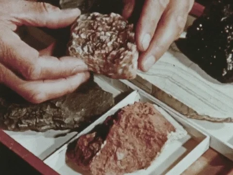 A gif of a person's hands turning over a sample of rock. More rock samples are in the background.