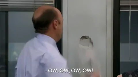 A man repeatedly punches a hole in a wall while saying OW.