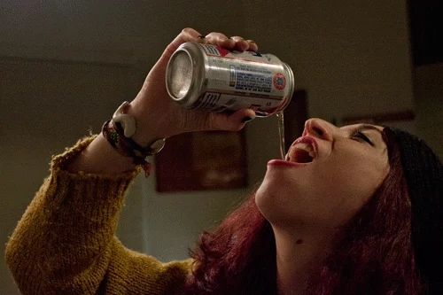 A woman drinking a can of beer or soda, letting it flow from the air into her mouth.