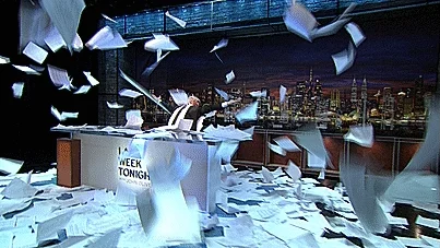 Papers flying everywhere creating a big mess around a newscaster, John Oliver 