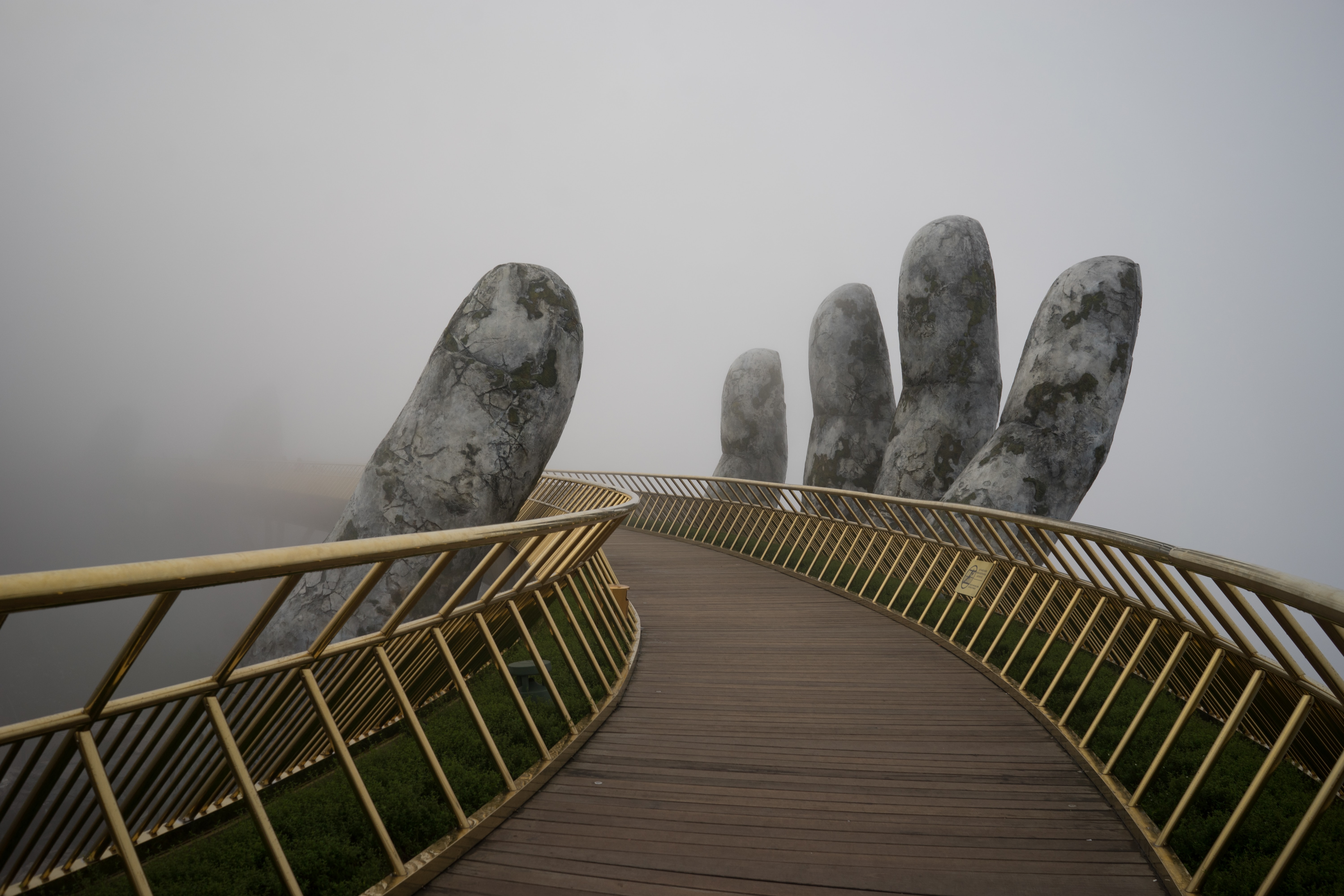 A bridge with a golden rail. A statue of a hand wraps around the bridge.