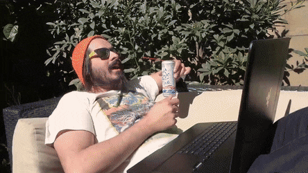 A man relaxing outside. His laptop rests in his lap while he stretches out.