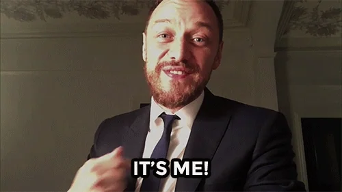 A man in a suit and tie smiling and saying, "It's me!"