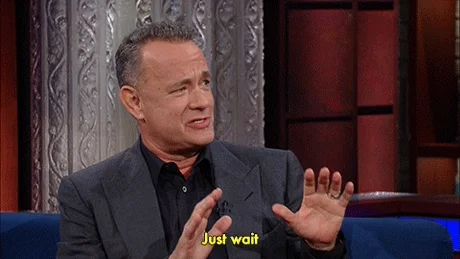 Actor Tom Hanks on a late night show saying, 'Just wait' with both hands pushing forward at shoulder level .