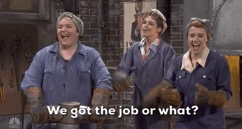 A group of women in work uniforms look surprised and happy. One of them says, “We got the job or what?”