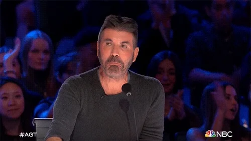 Simon Cowell nodding, impressed, at an America's Got Talent contestant as the audience applauds behind him.