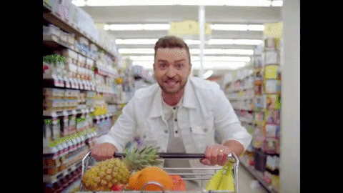 Justin Timberlake pushing a cart of veggies and fruits down an aisle at the grocery store