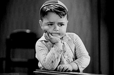 A young boy with a serious face, tapping a desk in deep thought.