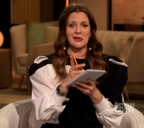 Drew Barrymore with a notepad, signalling for the audience to come to her. She starts writing on the notepad.