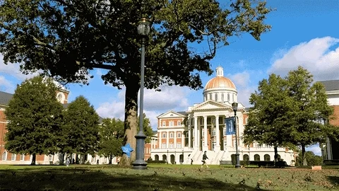 A time lapse of a college campus in the fall. Leaves blow across a field in front of a building.