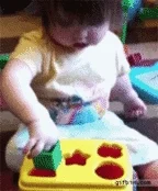 Child trying to put a square block into the circle hole on their shape sorter. Finally lifts the lid to put the shape inside.