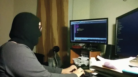 A hacker in a balaclava, sitting at a computer with multiple monitors. Typing, a third hand appears, and a banana. All typing