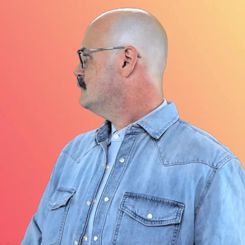 A man with a handlebar moustache looks around and points to himself. He asks, 