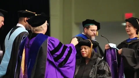 A woman in a hat and gown receiving a degree.