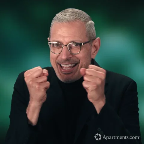 Jeff Goldblum, smiling and shaking his hands in excitement.
