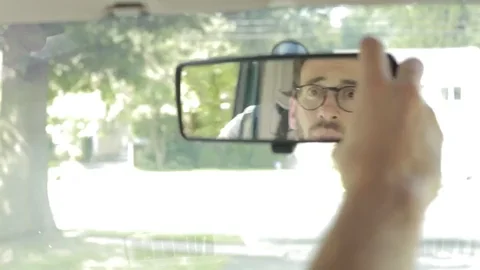 A man adjusting a car’s rearview mirror