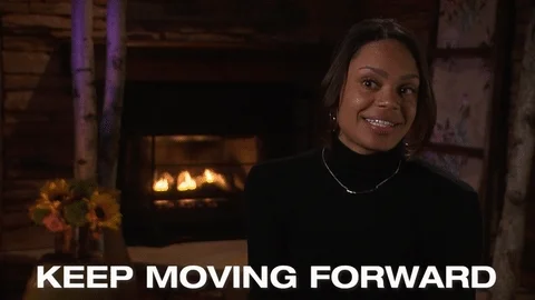 A woman sitting in front of a fireplace saying, 'Keep moving forward.' 