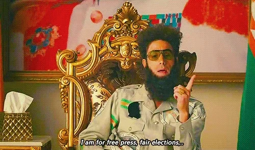 Sacha Baron Cohen character General Aladeen sitting on a golden throne, saying 