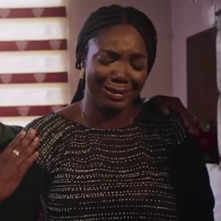 A woman shakes her head while crying, then raises the hand holding a tissue to touch her nose.