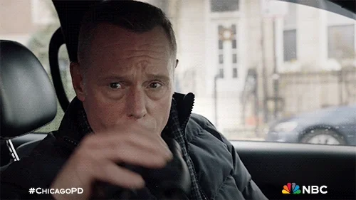 A man looks out a car window with binoculars. 