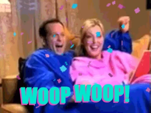 Couple dancing in snuggies, on the couch. He is wearing blue. She is wearing pink, reading a book. 