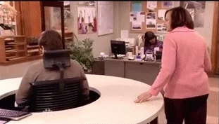 An office worker in a swivelling desk chair. He tries to ignore a coworker by turning his chair away.