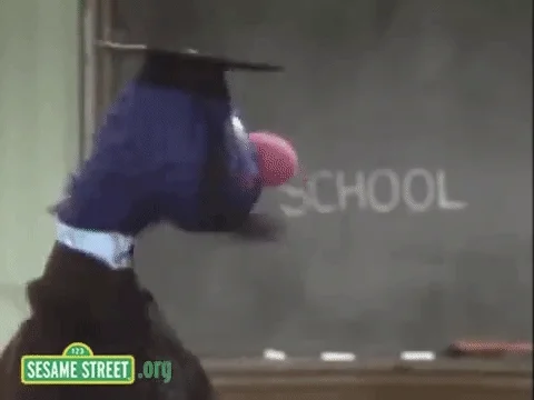 A sesame Street puppet in front of a chalkboard that reads, 