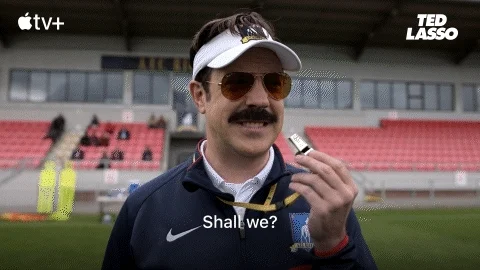 Ted Lasso blows a whistle on a soccer field. He says, 