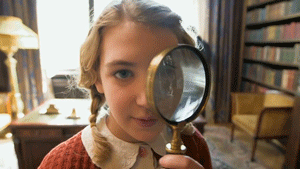 A girl in a library looking through a magnifying glass
