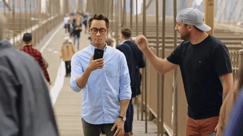 Man waving hand in front of distracted man on his phone. 