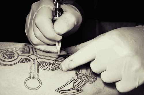 Gloved hands drawing a tattoo