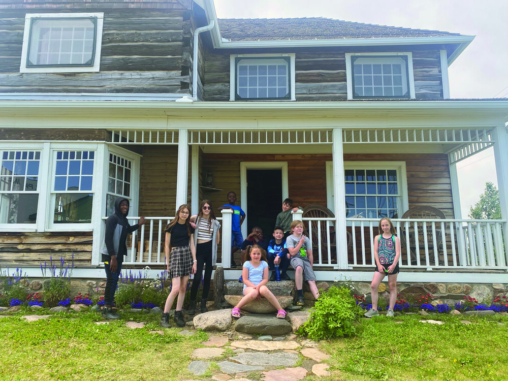 Ma «gang» devant la maison historique Destrubé au Musée de Saint-Paul : (de gauche à droite) Yan, Oriane, Solène, Jason (assis sur les marches), Éliott, Phaeton, Maysen, Eva (sur la roche devant), Jayden et Albert (devant la porte de la maison). Crédit : Virginie Dallaire