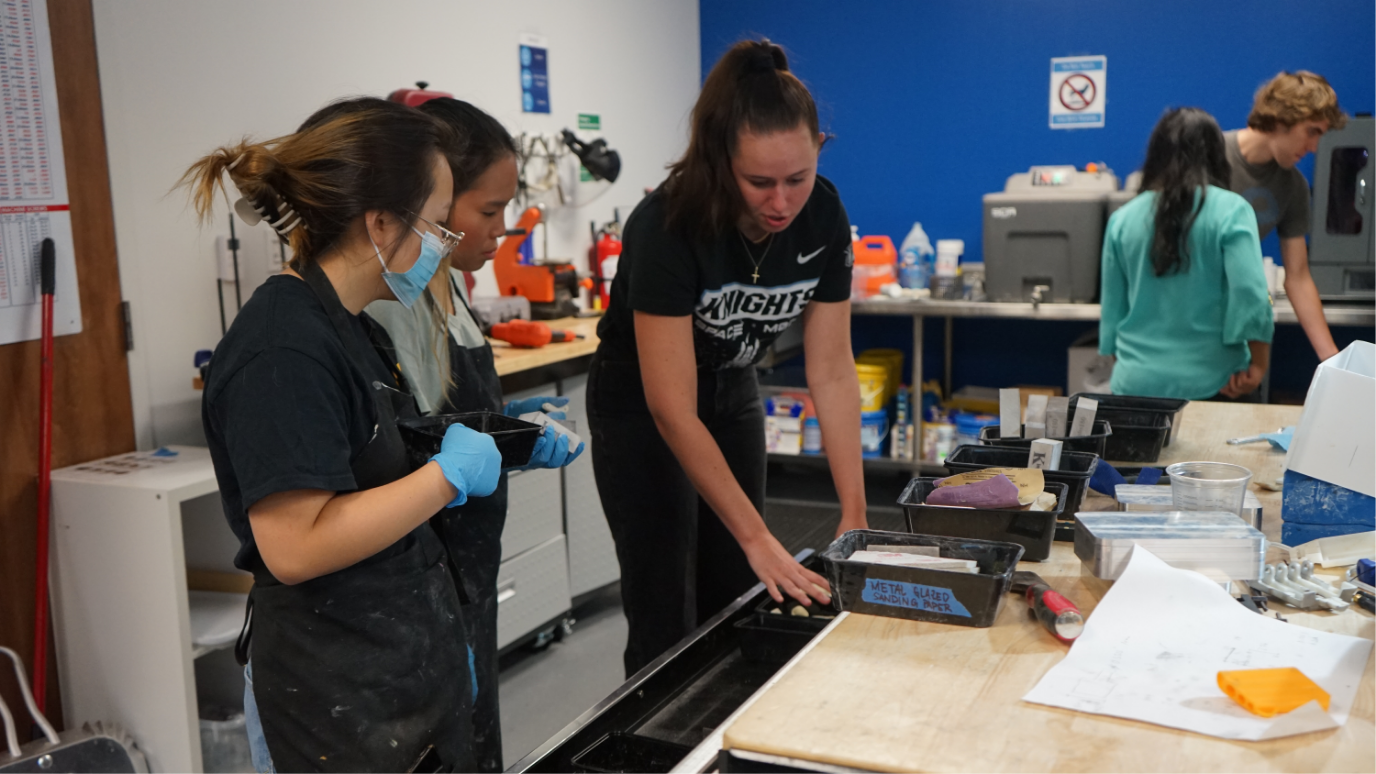 A bionic child getting her arm repaired and checked by a Limbitless student intern. Another student intern and the Limbitless president are pictured in the background.