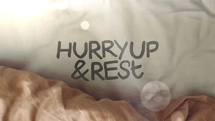 "Hurry Up & Rest" is written over a background of an unmade bed.
