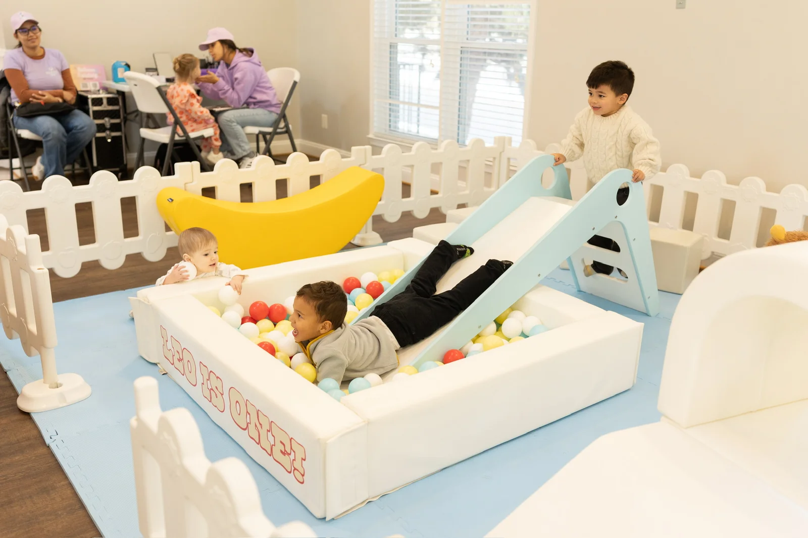 Kids playing in a soft play ball pit with slide during a first birthday celebration