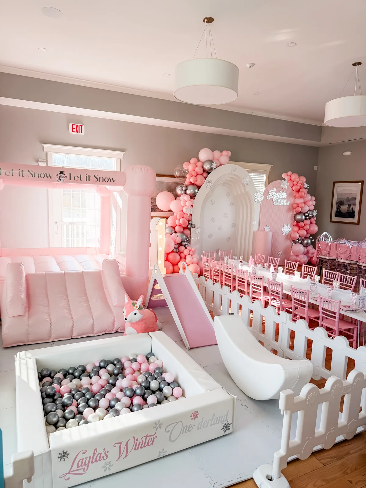 Winter wonderland birthday room with pink bounce house, ball pit, balloon arch, and banquet table