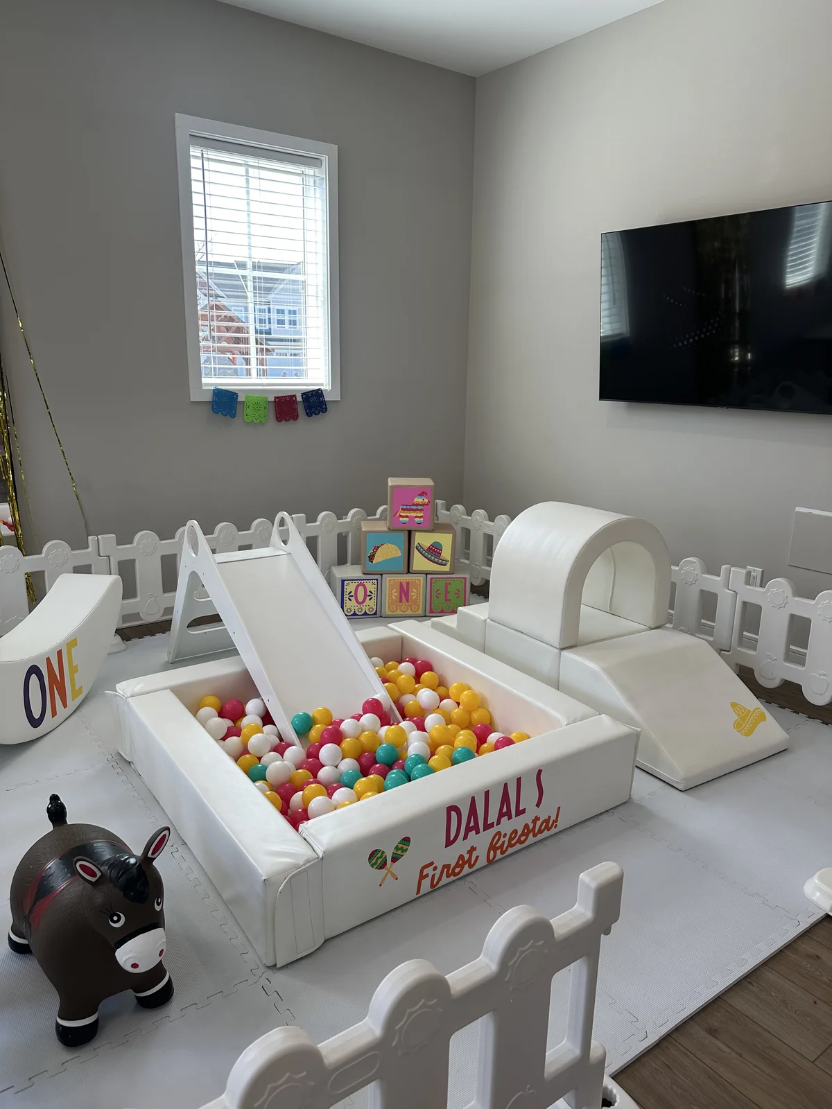 Indoor fiesta first birthday soft play with white ball pit, slide, and colorful blocks