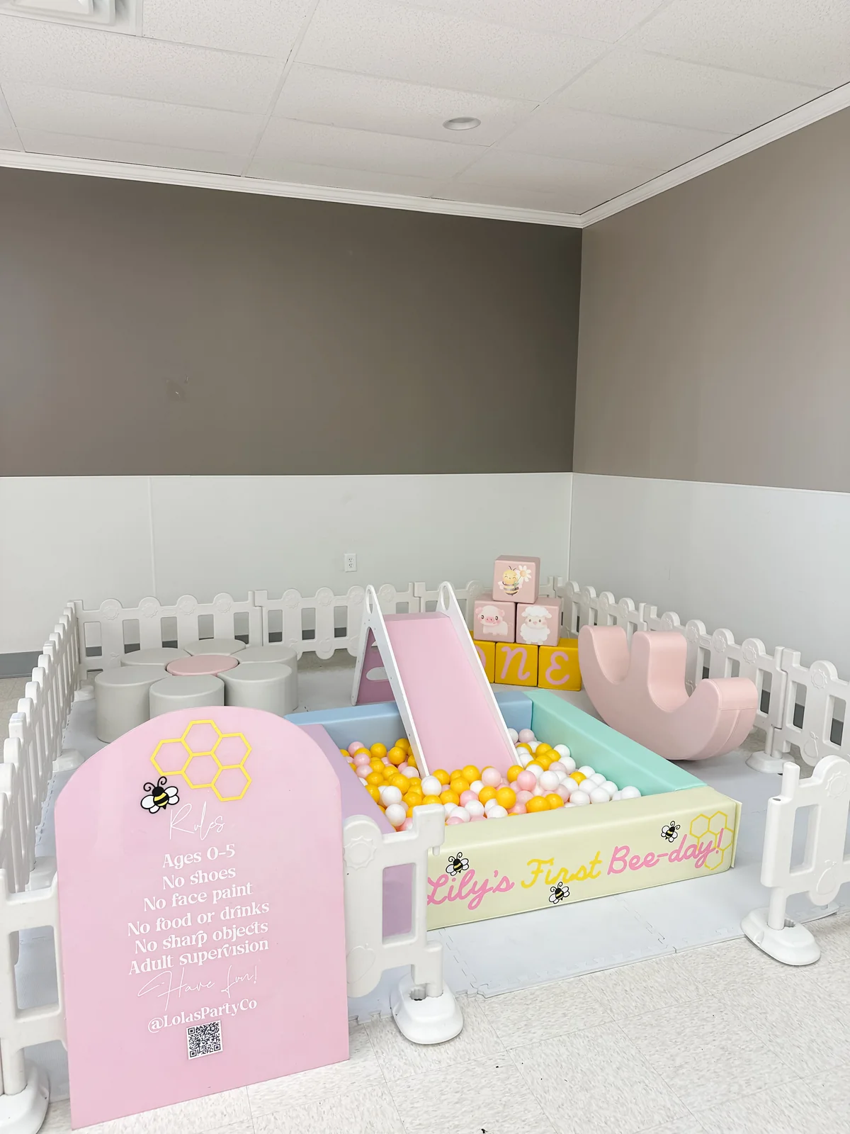 Bee-day themed soft play with pastel yellow ball pit, slide, and white picket fence
