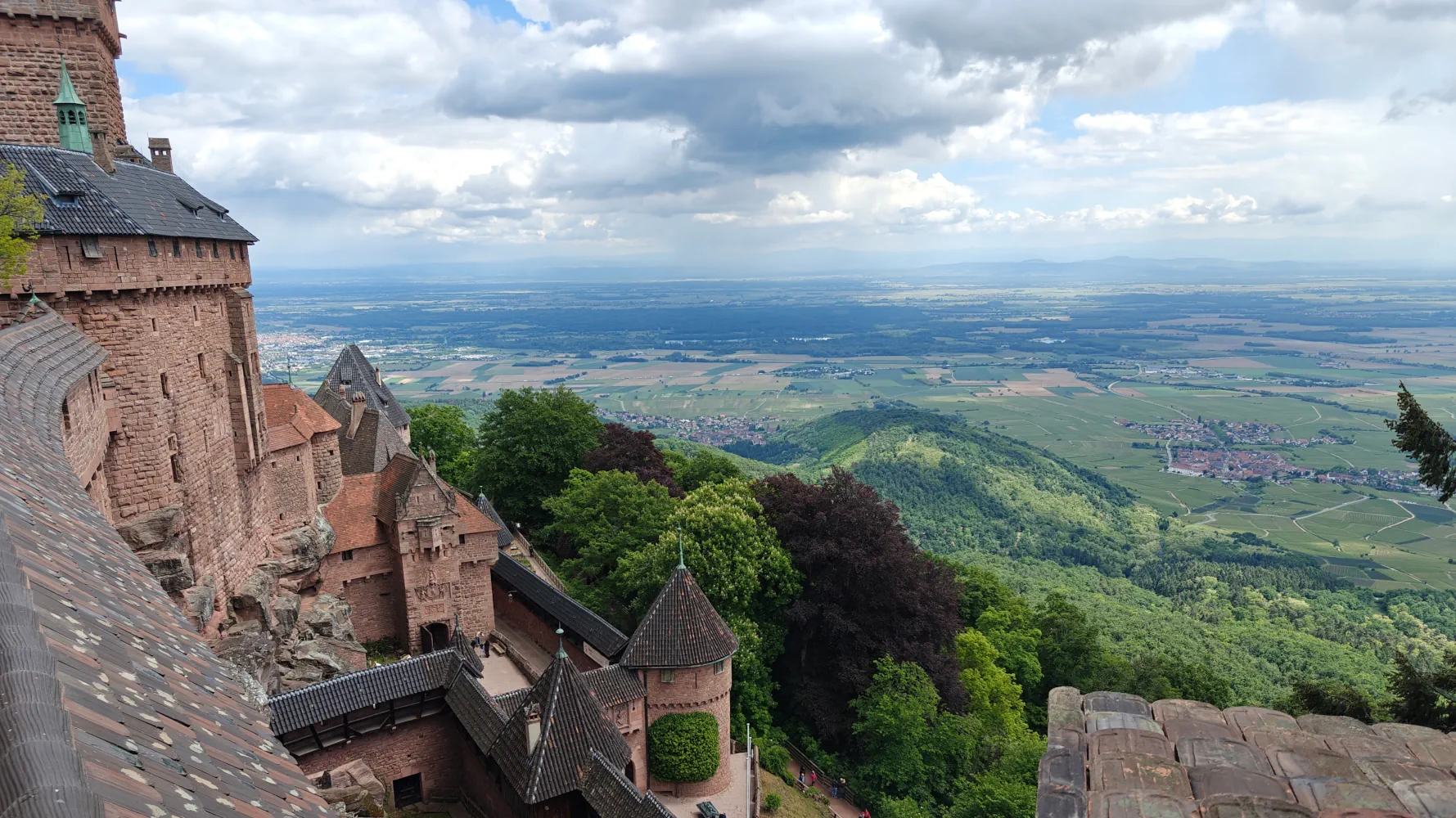 Taken from high up within the castle of Haut-Koenigsbourg, this photo captures some of the magnitude of the castle, with its many towers, sturdy walls, peaked roofs, and open windows look out over the valley between the Vosges and the Black Forest. Many small towns and expanses of forest are visible below.