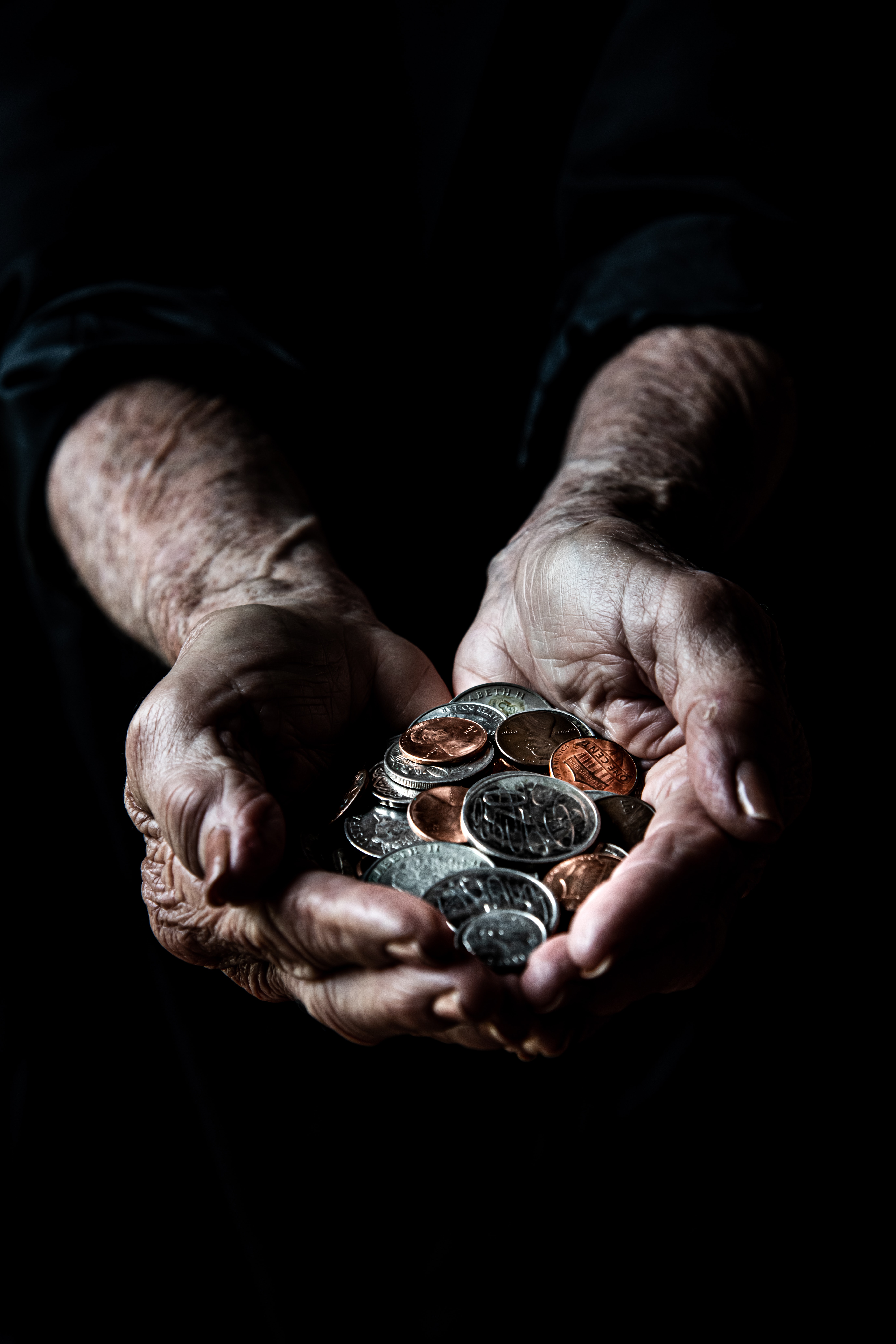 A photo of a pair of hands proffering a handful of coins to the viewer against a black background