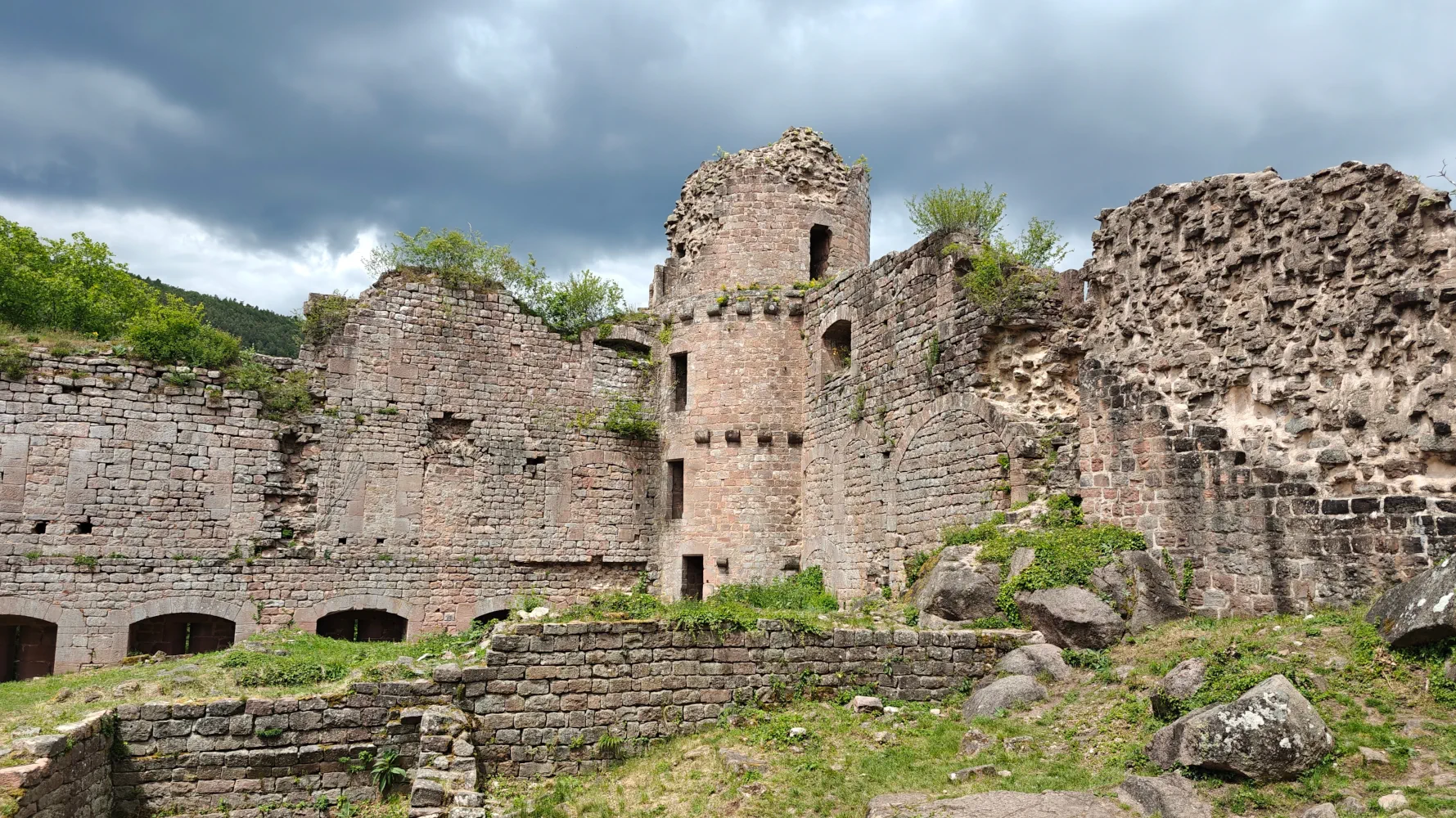 The ruins of the Landsberg Castle including crumbling round tower with tufts of moss and grass peeking out, all set against a dramatic gray sky.