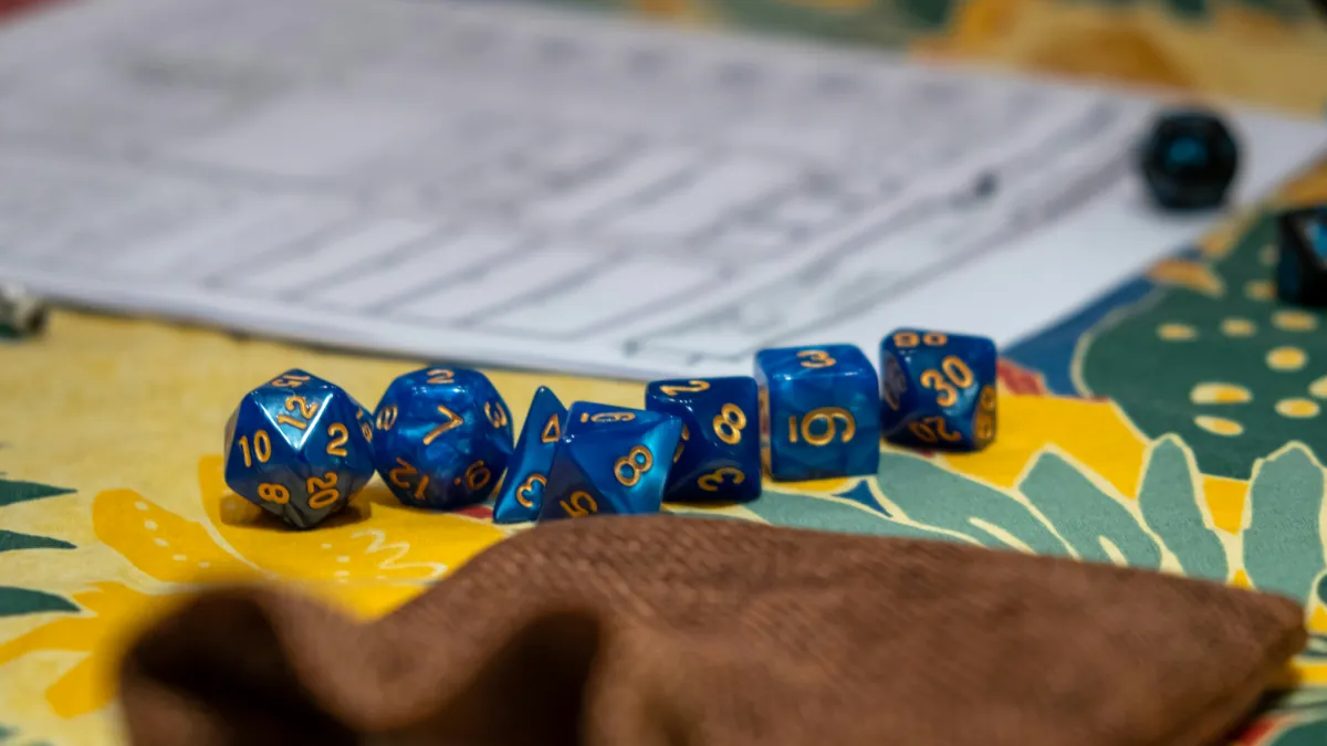 A set of blue dice is shown beside a brown cloth dice bag and in front of an RPG character sheet.