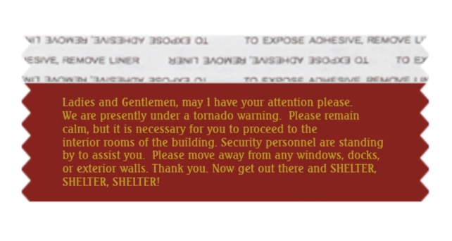 An image of a mock-up of a convention badge ribbon, which reads "Ladies and Gentlemen, may I have your attention please. We are presently under a tornado warning. Please remain calm, but it is necessary for you to proceed to the interior rooms of the building. Security personnel are standing by to assist you. Please move away from any windows, docks, or exterior walls. Thank you. Now get out there and shelter, shelter, shelter!"