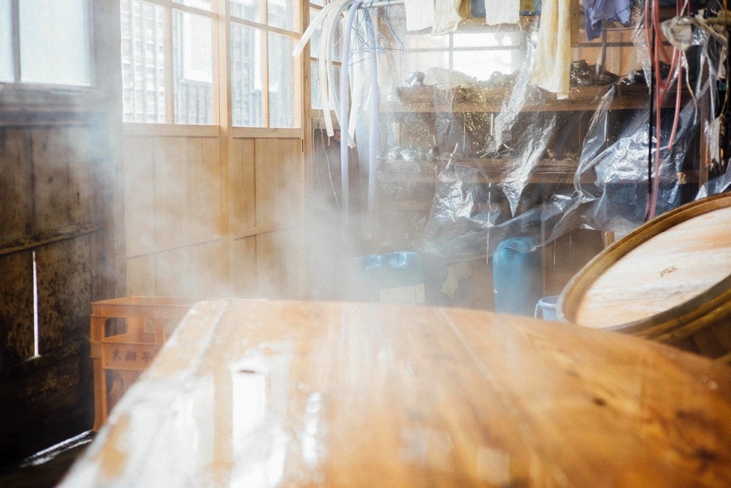 Steam rising inside the brewery near a wooden rice-steaming vessel