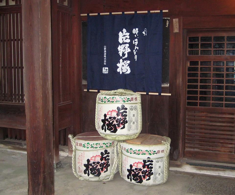 Sake barrels (taru) stacked at the brewery entrance beneath the Katano Sakura noren banner