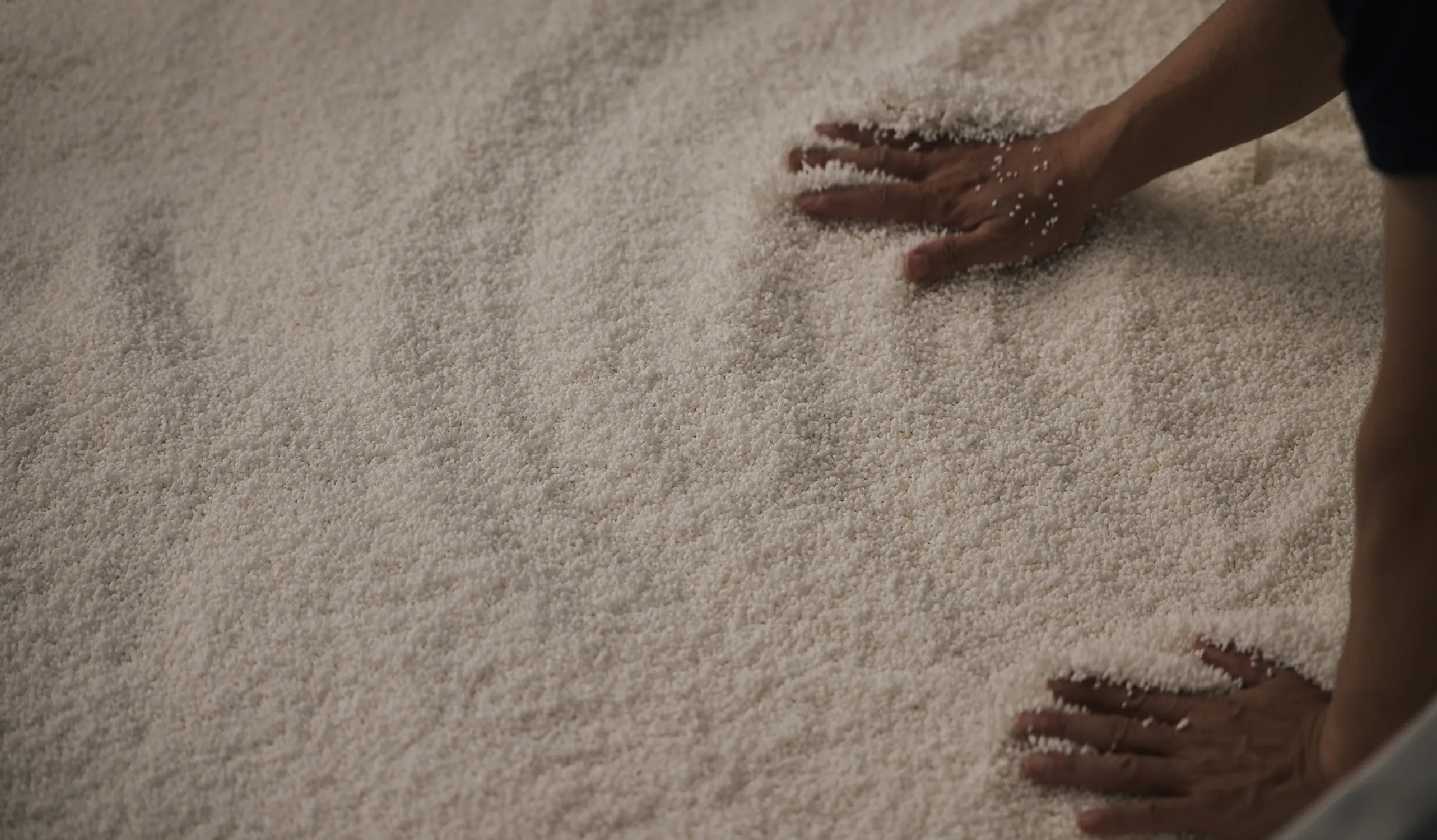 Hands working freshly steamed rice spread out during the brewing process.