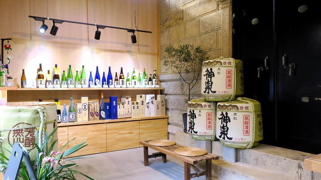 Interior of the brewery's direct-sale shop, with bottles displayed on shelves and Shinsen-branded sake barrels.
