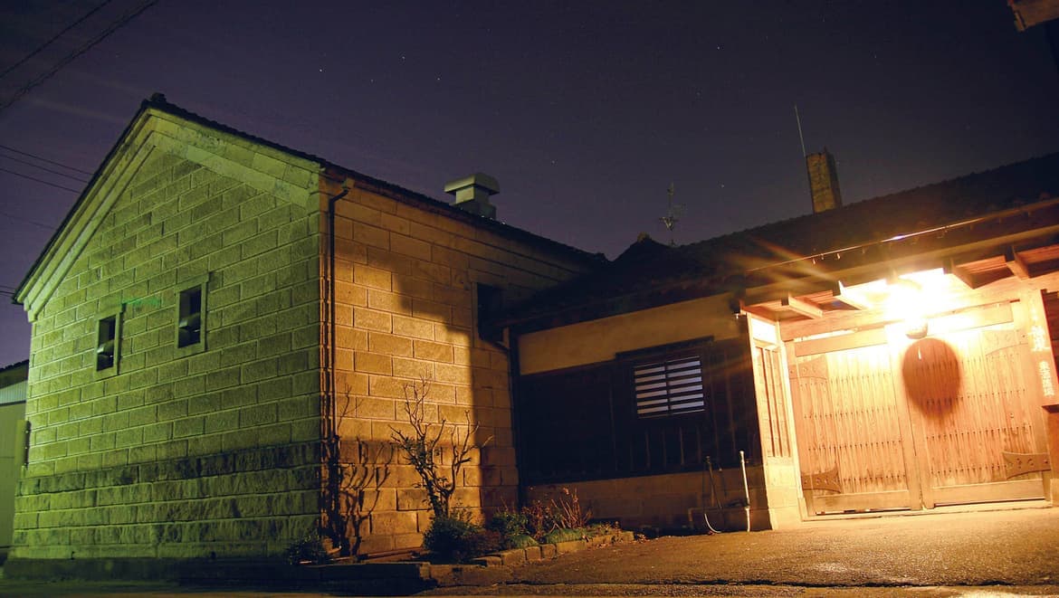 Night view of the brewery's stone storehouse and wooden gate, part of the registered tangible cultural property complex.