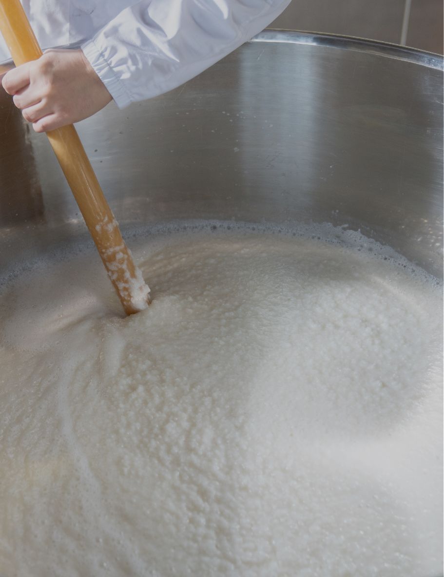 Fermenting moromi mash being stirred by hand in a brewing tank.